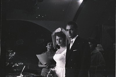 Black-and-white wedding portrait featuring a bride in a full veil and groom in formal attire, likely 1950s–1970s. Indoor sett...