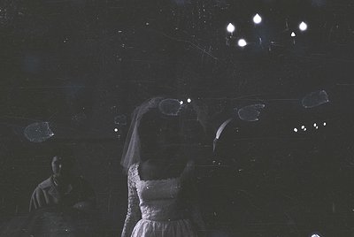 Black-and-white wedding portrait with dramatic lighting. Bride in flowing gown and veil, arms raised, under suspended geometr...