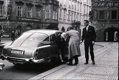 Classic 1950s-60s European street scene featuring a **Mercedes-Benz 300SL "Gullwing"** (RC-41-139 license) parked on cobblest...