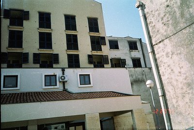 Mid-century urban building with Brutalist elements—exposed concrete, red-tiled roof overhang, and uniform rectangular windows...