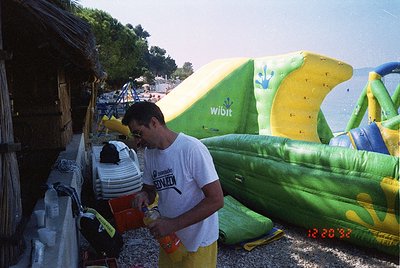 Retro beach scene featuring inflatable water sports equipment. A man in a white T-shirt with a "Wibit" logo on a banana-shape...