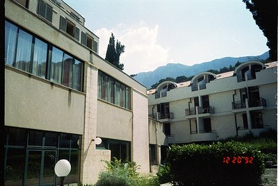 Mid-century modern apartment complex with flat roofs, large windows, and concrete/brick façade. Mountain backdrop suggests al...