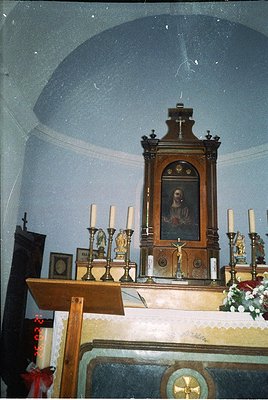 Ornate wooden iconostasis in a domed Orthodox church interior, featuring a central religious portrait framed by candle holder...