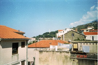 Vintage aerial view of Mediterranean hillside village with terracotta-tiled rooftops and whitewashed buildings. Laundry hangs...