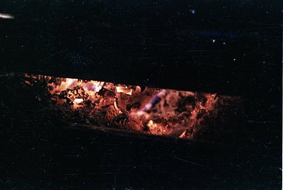 Intense close-up of a burning log fire in a dark setting, showcasing glowing embers and flickering flames. The scene captures...