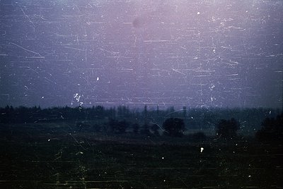 Vintage photograph showing a cracked, foggy windowpane with blurred forest and fields beyond. Heavy scratches and condensatio...