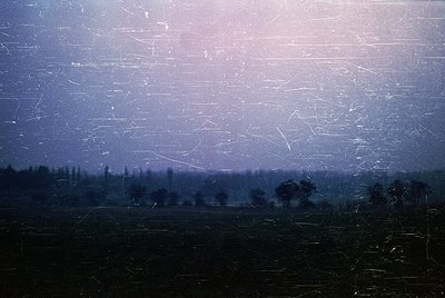 Vintage sepia-toned photograph of a rural landscape through cracked, aged glass. Distorted trees and fields suggest a nostalg...