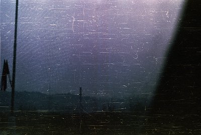 Vintage close-up of a scratched, fogged glass pane with faint reflections—likely a train window. Distorted silhouettes sugges...