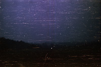 Vintage long-exposure night photography capturing light trails from passing vehicles on a rural road. Silhouetted trees frame...