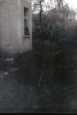 Vintage wet-plate photograph of a decaying concrete building corner with visible cracks and erosion. A small balcony with a s...