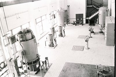 Industrial facility featuring mid-20th century machinery: large cylindrical tanks, valves, and piping in a spacious, concrete...