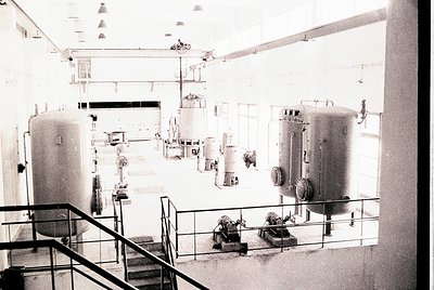 Industrial facility featuring mid-20th century pressure tanks, valves, and piping. High ceilings with exposed beams and stair...