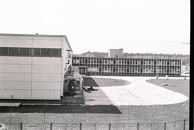 Mid-century Brutalist institutional building complex with raw concrete facade and extensive window bands. Courtyard area with...