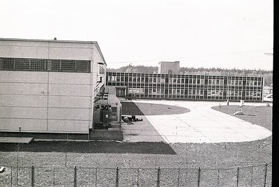 Mid-century Brutalist-style institutional building complex with raw concrete façade and grid-patterned windows. Courtyard are...