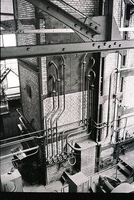 Industrial-era distillery interior featuring copper stills, brass valves, and intricate piping network. Brick walls and metal...