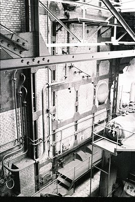 Industrial brick building interior with exposed steam pipes, scaffolding, and large circular/rectangular openings. Likely a 2...