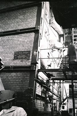 Industrial brick stairwell with exposed pipes, scaffolding, and a plaque reading *"The Old Factory"* (likely Soviet-era or Ea...