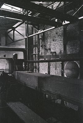 Industrial warehouse interior with exposed brick walls and high ceilings. Large metal beams and pipes dominate the space, sug...