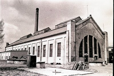 Industrial-era brick building with Art Deco-inspired arched entrance and tall chimney stack. Exterior shows signs of aging, w...