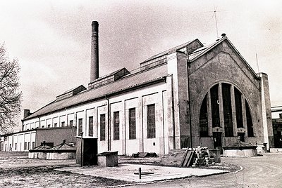 Industrial-era brick building with Art Deco-inspired arched entrance and tall chimney stack, likely a factory or power plant....
