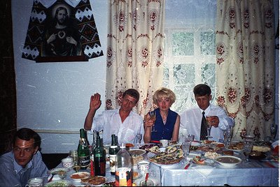 Vintage indoor gathering featuring four adults seated at a long table laden with seafood, bottles, and glasses. Decor include...