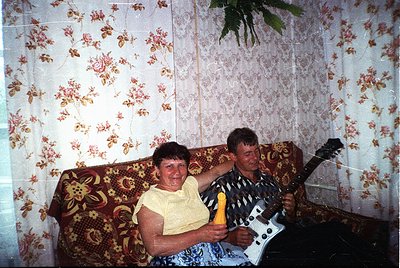 Vintage indoor portrait featuring two individuals in a patterned floral sofa setting, likely Eastern European 1980s-90s. Man ...