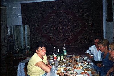 Vintage indoor gathering featuring a long dining table laden with seafood platters, bottles, and glasses. Three adults seated...