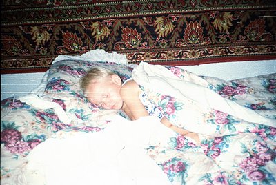 Child resting on floral-patterned bedding with ornate wallpaper featuring floral and animal motifs, likely mid-20th century i...
