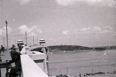 Vintage seaside promenade with Soviet-era architecture. White balustrade overlooks calm waters; small pavilion with dome roof...