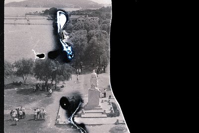 Vintage aerial photo of a public square with a prominent statue pedestal and figures in mid-20th century attire. Agricultural...