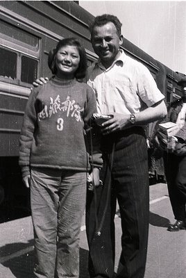 Black-and-white photo of two individuals posing near a vintage train car, likely mid-20th century. The woman wears a sweater ...
