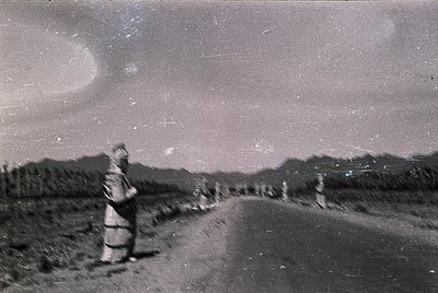 Vintage black-and-white photo of a lone figure in traditional alpine attire walking a narrow mountain road under a starry nig...