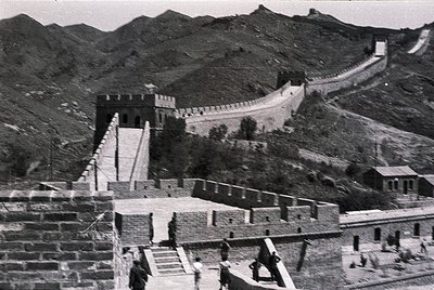 Historic black-and-white photo of the Great Wall of China, showcasing its iconic stone construction and watchtowers. The wind...