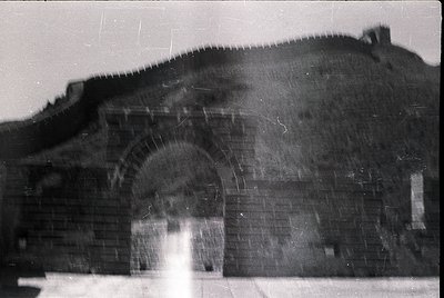 Vintage black-and-white photo of a large, arched brick gateway with weathered stonework. The archway appears to be part of a ...