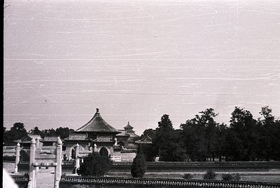 Vintage black-and-white photo of traditional Chinese pavilion with upturned eaves, surrounded by dense greenery and a low sto...