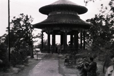 Vintage black-and-white photo of a multi-tiered pavilion with curved, tiled roof and ornate wooden columns, likely East Asian...