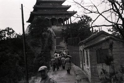 Vintage black-and-white photo of a traditional East Asian pagoda-style tower with tiered, curved eaves. A group of people in ...