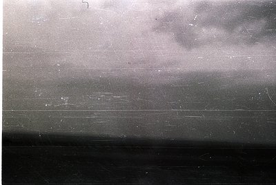 Vintage black-and-white photo of a train window showing blurred motion and light reflections. Horizontal scratches and slight...