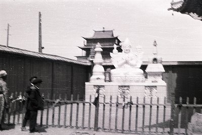 Vintage black-and-white photo of a traditional East Asian architectural gate with tiled pagoda roof, flanked by stone lion st...