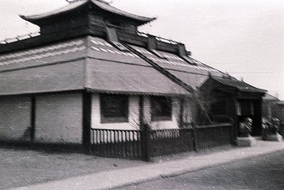 Vintage black-and-white photo of a traditional East Asian-style building with tiled roofs and ornate eaves, likely mid-20th c...