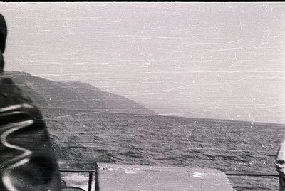 Vintage black-and-white shot of a person standing on a high vantage point overlooking a rugged coastline. Distinctive vertica...