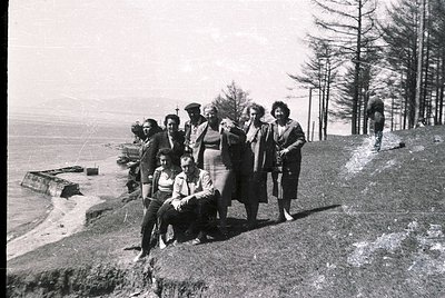 Black-and-white group photo on rocky seaside cliff, likely Bulgaria’s Black Sea coast. Nine individuals pose on uneven terrai...