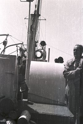 Mid-20th century fishing vessel with vintage navigation equipment: round porthole, lantern, and rigging. Man in dark suit sta...