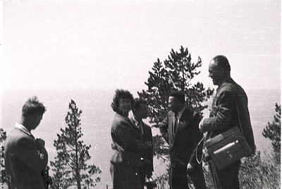 Black-and-white group portrait of five individuals in outdoor setting, likely mid-20th century. Four men in suits and one wom...