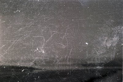 Close-up of weathered, scratched metal surface with faint graffiti-like markings. Likely industrial or urban setting, suggest...