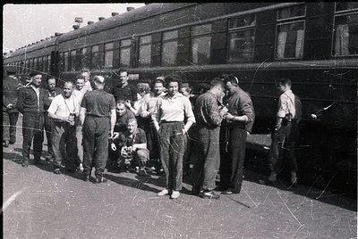 Vintage black-and-white photo of a group of men posing near a mid-20th-century passenger train, likely 1950s–1960s. Uniform w...