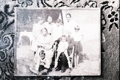 Vintage black-and-white family portrait from the early-to-mid 20th century, likely 1940s–1950s. Nine individuals pose indoors...