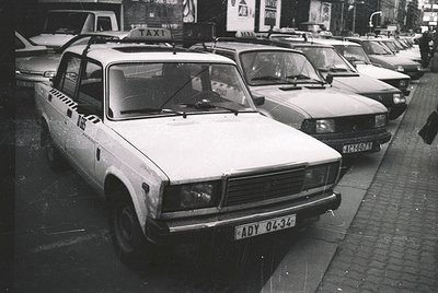 Vintage taxi fleet in urban setting, featuring a prominent Lada taxi (ADY 04-34) with "TAXI" signage and black-and-white chec...