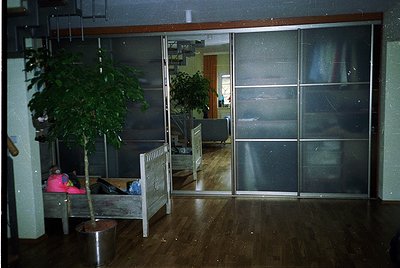 Mid-century modern interior with sliding glass partitions, reflecting a minimalist office or waiting area. Wooden floor, pott...