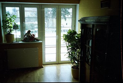 Mid-century interior with sliding glass doors revealing a snowy courtyard. A child sits on a built-in bench beside a potted p...